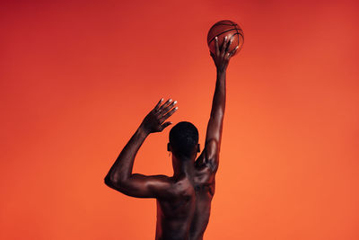 Rear view of shirtless man standing against red background