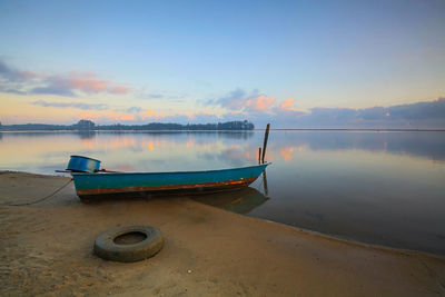 Boat moored on beach against sky during sunset