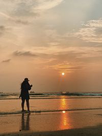 Rear view of woman standing on shore at beach during sunset