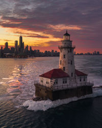 Lighthouse by sea against sky during sunset