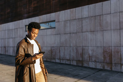 Man using mobile phone while standing against building