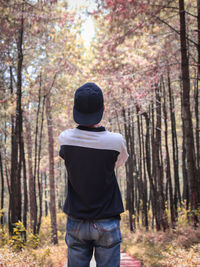 Rear view of man standing by trees in forest