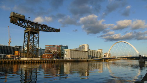 Cranes by river against sky in city