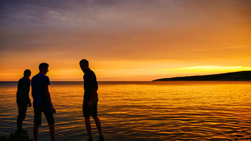 Silhouette people standing on beach against sky during sunset