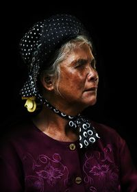 Close-up of senior woman looking away against black background