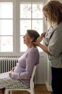 Side view of young female nurse brushing senior woman's hair at retirement home