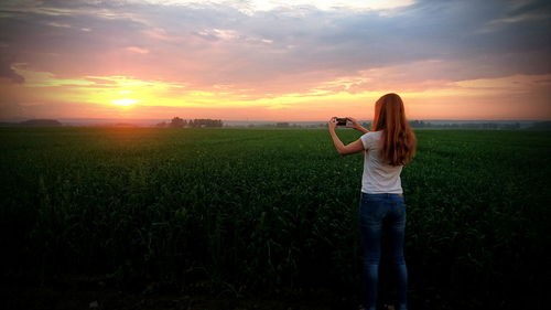 Woman photographing field against sky during sunset