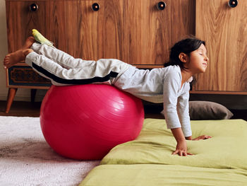 Full length of girl exercising with fitness ball at home