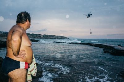 Rear view of shirtless man standing in sea against sky