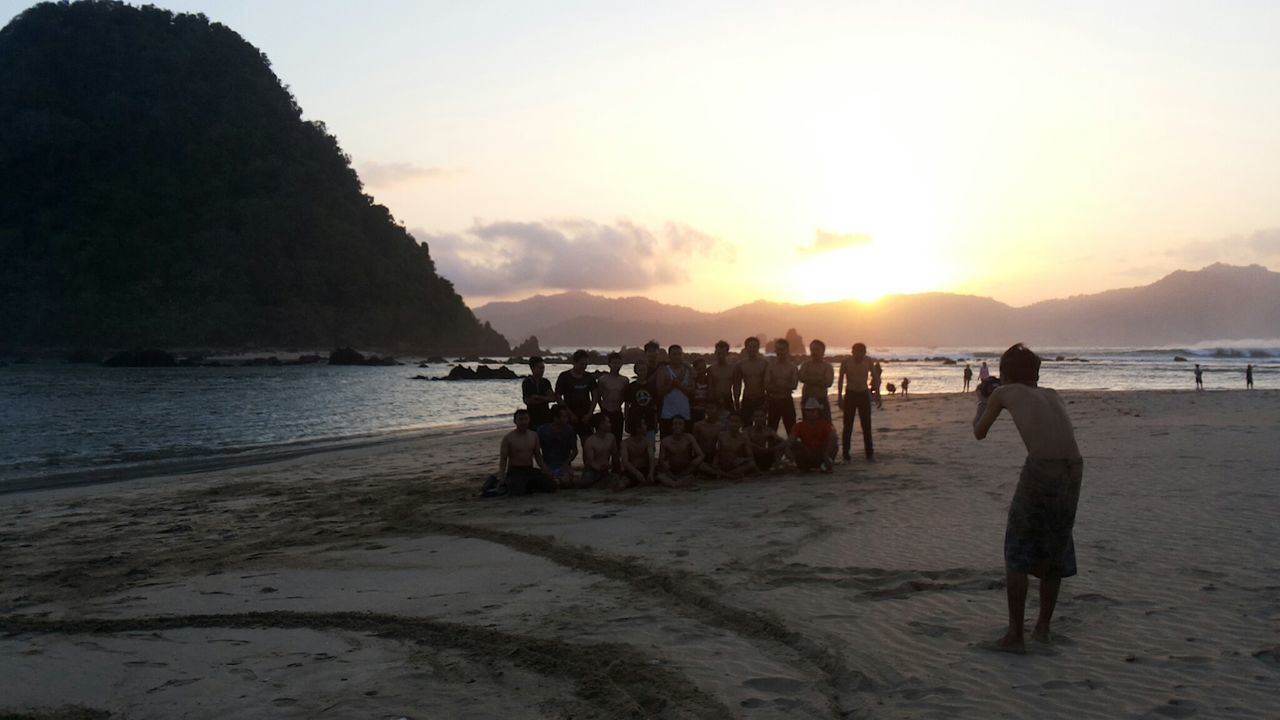 GROUP OF PEOPLE ON BEACH AGAINST SKY DURING SUNSET