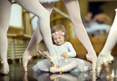 Little ballerina tying pointe shoes for adults