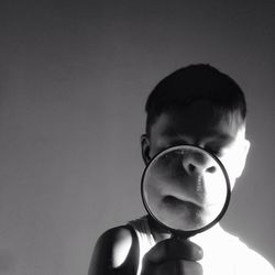 Boy holding magnifying glass against wall