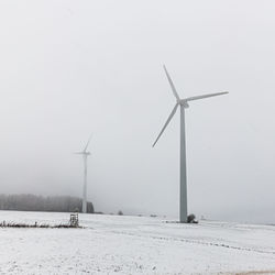 Windmills on snow covered field against sky