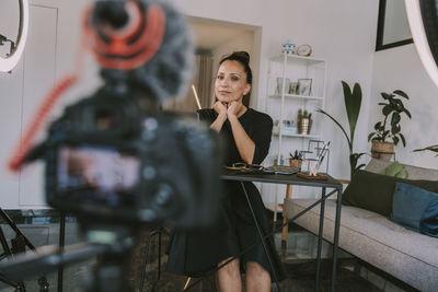 Businesswoman with hand on chin vlogging at home