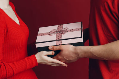 Midsection of couple holding gift box against red background