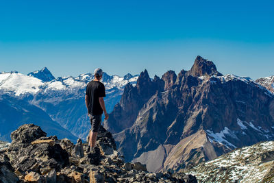 Rear view of man standing on mountain against clear blue sky