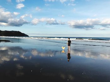 Rear view of boy with dog walking on beach against sky