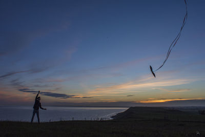 Silhouette man flying kite against sky during sunset