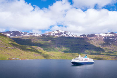 Blue and white cruising ship in a fjord of seydisfjordur, iceland, on a partly cloudy day.