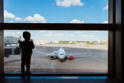 Rear view of man standing on airport runway against sky