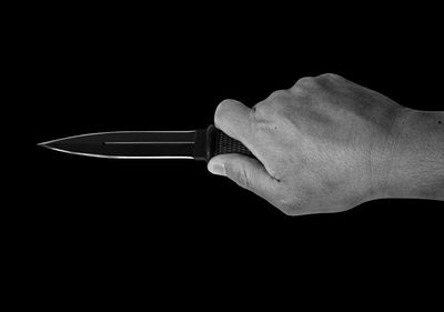 Close-up of hand holding metal against black background