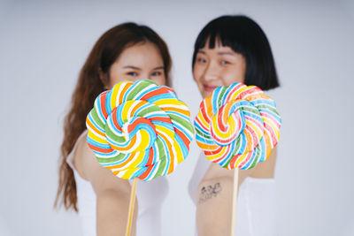 Portrait of lesbian couple holding lollipop against white background