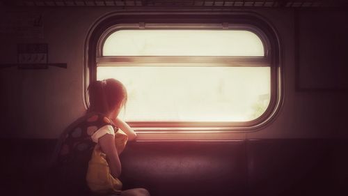 Side view of young woman looking through window while traveling in train
