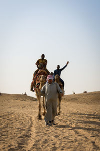 Men riding horse on sand against clear sky