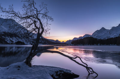 Scenic view of lake by snowcapped mountains against sky during sunset