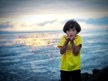 Cute girl blowing confetti at beach during sunset