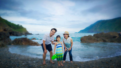 Father and daughter standing on beach against sky