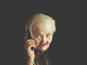 Portrait of senior woman talking on smart phone against black background