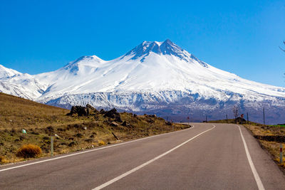 Road leading towards snowcapped mountain against blue sky