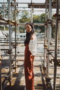 Portrait of beautiful woman standing by metallic built structure