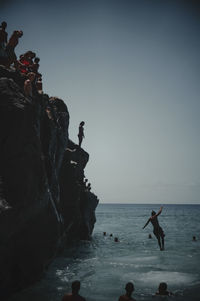 People on rocks by sea against sky