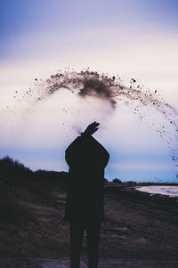 Rear view of silhouette man standing on beach against sky during sunset