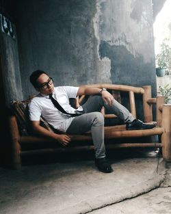 Man looking away while sitting on bench against wall