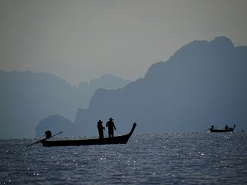 Silhouette people on boat in sea against sky