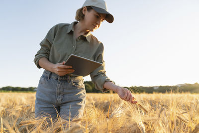 Woman holding digital tablet in field examining barley ear