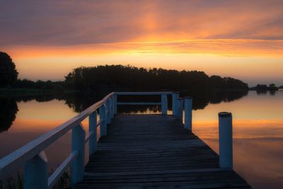 Pier over lake against romantic sky at sunset