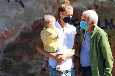 Rear view of grandfather, daughter wearing coronavirus mask and grandson  on the street