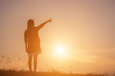 Silhouette woman standing on field against sky during sunset