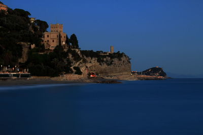 Buildings by sea against clear blue sky