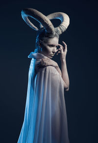 Woman with body paint and horns standing against black background