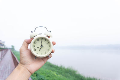 Human hand holding clock against the sky