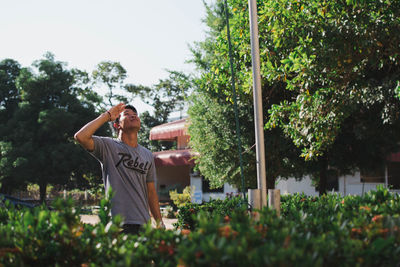 Young man looking up and saluting while standing by plants