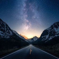 Empty road amidst mountains against sky at night