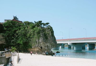 People on beach by bridge against clear sky