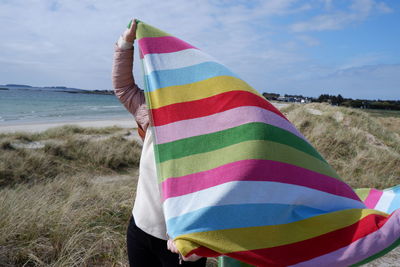 Low section of person holding towel on beach against sky