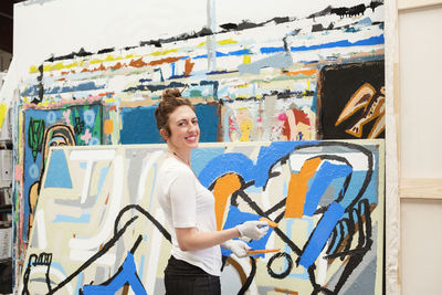 Portrait of happy female artist painting in studio